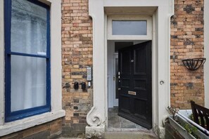 Une maison traditionnelle en briques, avec une porte d’entrée noire, une sonnette blanche et une boîte aux lettres fixée au mur de briques.