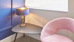 A corner room with a small round table, a pink chair, and a lamp. - Anya’s Lookout - 1 Bedroom Apartment In Scarbourgh (North Yorkshire)