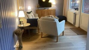 A modern living room with a sofa, armchairs, a TV, and a small table with lamps. - 4 Star Holiday Home in Norre Nebel (Norre Nebel)