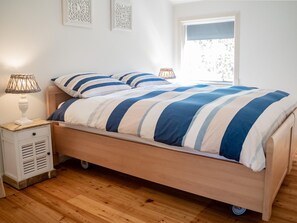 A single bed with a striped bedspread, a bedside table with a lamp, and a window with a view of trees. - Seaside Escape With Comfort (Paesens)