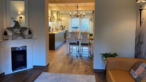 A modern living room with a fireplace, a dining area with wooden chairs, and a kitchen in the background. - Seaside Escape With Comfort (Paesens)