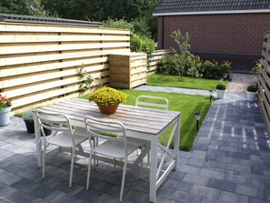 A patio with a wooden table and white chairs, surrounded by a wooden fence and a small garden. - Seaside Escape With Comfort (Paesens)