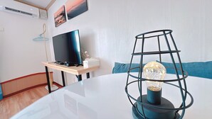 Una habitación moderna con una mesa de vidrio, un televisor sobre un soporte de madera, una lámpara decorativa y una almohada azul.