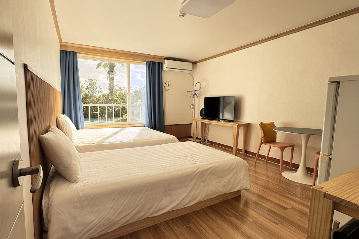 A hotel room with a large bed, a desk with a TV, a chair, and a balcony with a view.