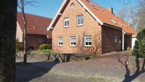 Une maison à deux étages, construite en briques, avec un toit recouvert de tuiles rouges, de nombreuses fenêtres et une allée pavée.