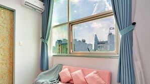 A room with a pink sofa, a window with curtains, and an air conditioning unit on the wall. - HANZ Vivianne Boutique Hotel (Ho Chi Minh City)