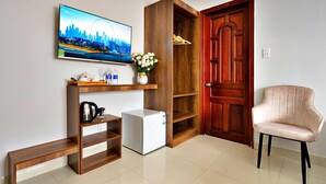 A compact living space with a television mounted on the wall, a small refrigerator, a wooden cabinet with shelves, a door, and a chair. - HANZ Vivianne Boutique Hotel (Ho Chi Minh City)