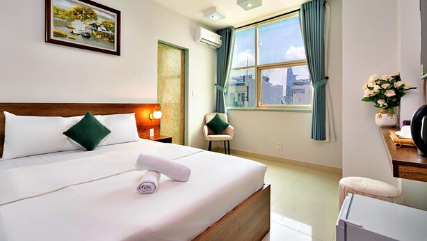 A hotel room with a neatly made bed, a chair, a desk with a computer, a window with curtains, and an air conditioning unit. - HANZ Vivianne Boutique Hotel (Ho Chi Minh City)