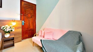 A room with a wooden door, a pink sofa, a small table with a vase of flowers, and a wall-mounted light fixture. - HANZ Vivianne Boutique Hotel (Ho Chi Minh City)