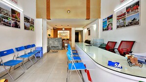 A hotel lobby with a long reception desk, blue folding chairs, a clock, and a wall with photos. - HANZ Vivianne Boutique Hotel (Ho Chi Minh City)