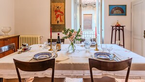 En spisestue med et bord dækket til to, med en vase blomster, en flaske vin og et traditionelt kinesisk maleri på væggen.