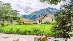 An outdoor dining area with a table set for two, surrounded by lush greenery and a mountain backdrop. - Regina 29 by Interhome (Tremezzina)