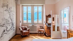A bedroom with a bed, a chair, a dresser, and a large window with a mountain view. - Regina 29 by Interhome (Tremezzina)