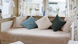 A cozy room with a sofa adorned with textured pillows, a small table with glasses, and a view of the outside through a window with a view of buildings and a bird feeder. - 4 Person Holiday Home in Falkenberg-by Traum (Falkenberg)