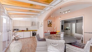A modern kitchen with white cabinets, a dining area with wicker furniture, and a large window providing natural light.