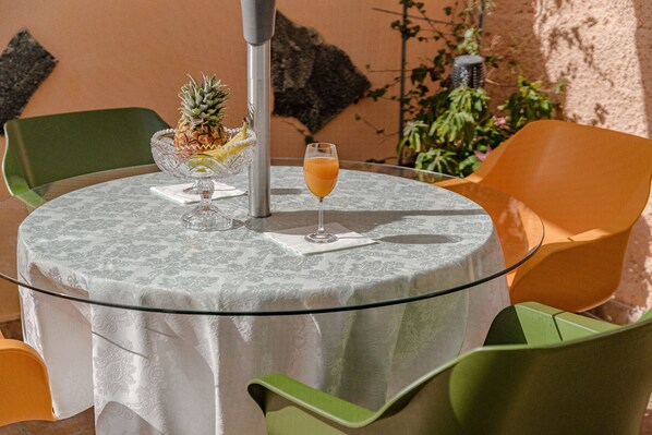 A round table with a glass top, surrounded by green chairs, and a glass of orange juice.