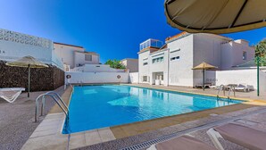 A swimming pool with lounge chairs and umbrellas, surrounded by buildings with white walls and red-tiled roofs.