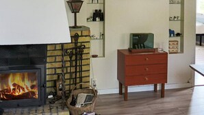 A cozy living room with a fireplace, a wicker basket, a wooden dresser, and a shelf with various items. - 6 Person Holiday Home in Varberg-by Traum (Varberg)