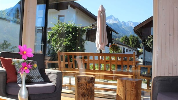 A cozy outdoor seating area with a wooden bench, a cushioned chair, and a wooden table. A vase with flowers is on the table. - Ferienwohnung Mondholz (Garmisch-Partenkirchen)