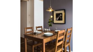 A dining area with a wooden table, four chairs, a hanging light fixture, and a framed picture on the wall. - Ferienwohnung Mondholz (Garmisch-Partenkirchen)