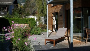 A wooden deck with a lounge chair, a balcony with metal railings, and a mountain backdrop. - Ferienwohnung Mondholz (Garmisch-Partenkirchen)