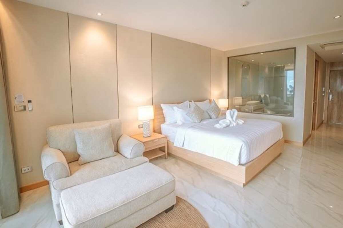 A modern bedroom with a bed, a sofa, a nightstand, and a large mirror.