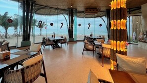 Un restaurant situé en bord de mer, avec des tables et des chaises, de grandes fenêtres donnant sur la plage et un plafond en bois.