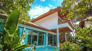 Une maison moderne dotée d’une grande porte vitrée, d’une piscine et d’une végétation tropicale luxuriante.