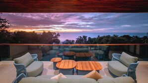 Un espace extérieur moderne, aménagé avec des meubles en osier et des tables en bois, offrant une vue imprenable sur un magnifique coucher de soleil.