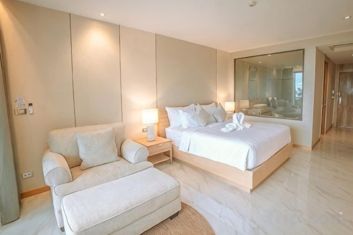 Una habitación de hotel moderna con una cama grande, un sofá, una mesita de noche y un espejo.