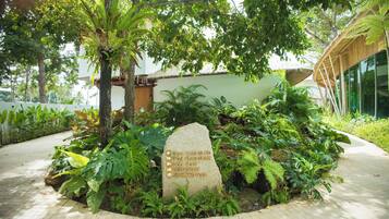 A stone sign with directions to Villa V107, Villa V104, Villa V107, a restaurant, and a swimming pool, surrounded by lush greenery and a paved walkway.