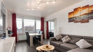 Un salon moderne avec un canapé gris, une table basse ronde et un coin repas comprenant une table et des chaises blanches.