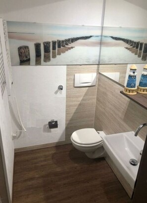 A compact bathroom with a toilet, sink, and a decorative mural of a beach scene. - Apartment Albatros 14 (Butjadingen)