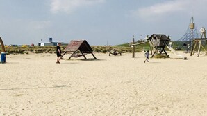 A sandy beach with a wooden structure, possibly a beach hut, and a playground with a slide. - Apartment Albatros 14 (Butjadingen)