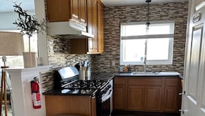 A kitchen with wooden cabinets, a stainless steel trash can, a gas stove, and a stone backsplash.