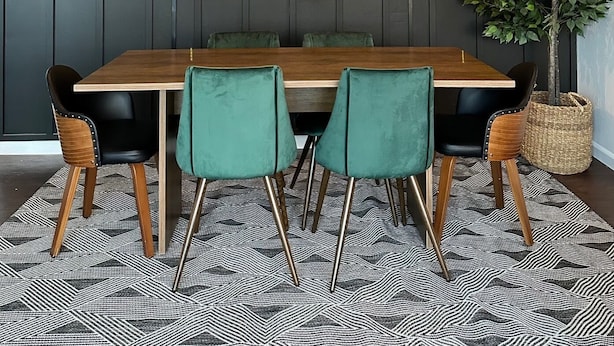 A dining area with a wooden table, green upholstered chairs, and two wall-mounted pendant lights.