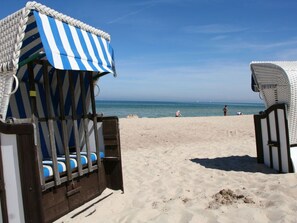 En strand med en randig strandstol och ett vitt strandparasoll.