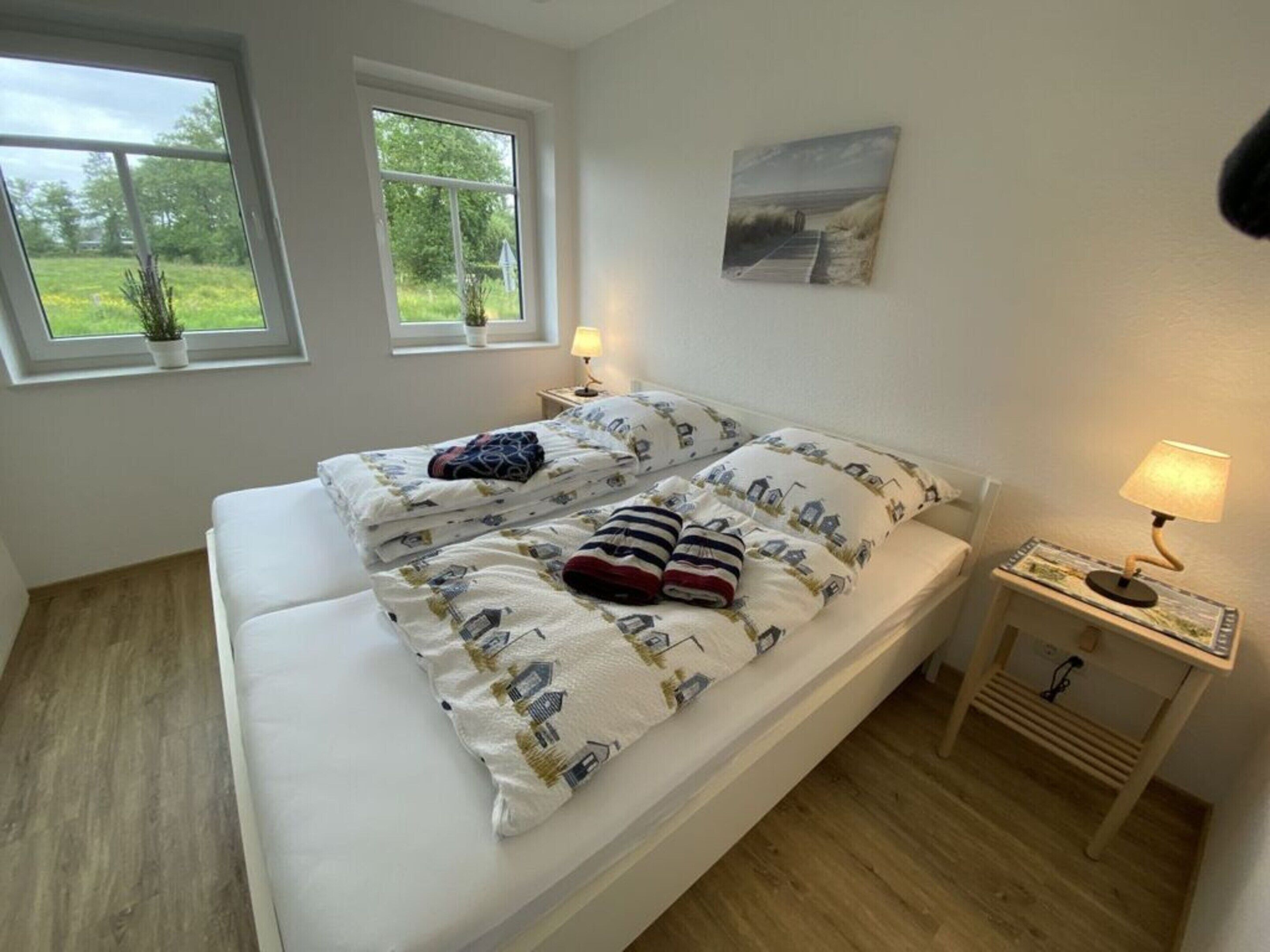 Ein Einzelbett mit weißer Matratze und einem gemusterten Überbett, zwei Nachttischlampen, ein kleiner Tisch mit einer Lampe sowie ein Gemälde an der Wand.