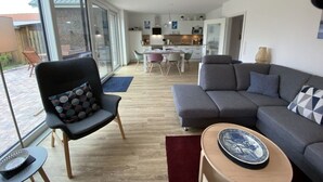 A modern living room with a grey sofa, a patterned armchair, and a dining area with a table and chairs. - Holiday Home on Bornfeld (Osteel)