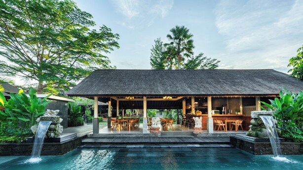 A poolside area with a covered seating area, a waterfall feature, and lush greenery. - PURI ANDONG VILLAS (Ubud)
