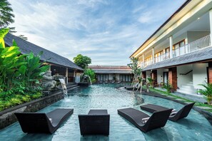 A pool area with lounge chairs, a waterfall feature, and a building with a balcony. - PURI ANDONG VILLAS (Ubud)