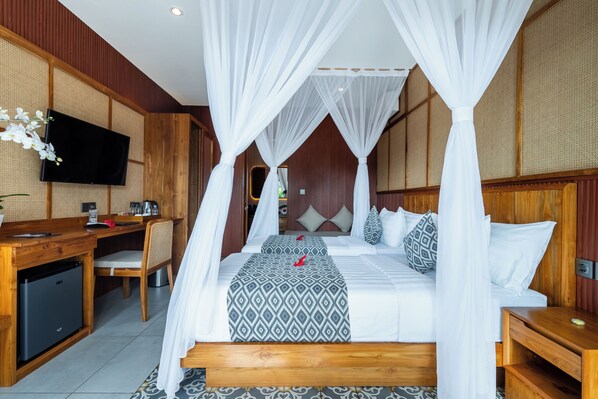 Una habitación con una cama bajo un dosel, un escritorio con una silla, un televisor y un refrigerador pequeño.