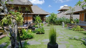 A tropical resort with thatched-roof bungalows, a well-maintained garden, and a clear blue sky. - PURI ANDONG VILLAS (Ubud)