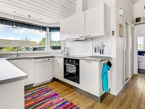 Une cuisine moderne avec des meubles blancs, un four encastré et un tapis aux couleurs vives.