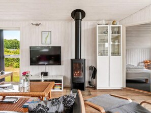 A cozy living room with a fireplace, a flat-screen TV, and a dining area with a wicker table and chairs.