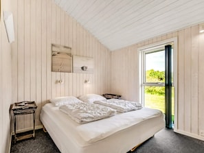 A bedroom with a bed, a nightstand, a window, and a wall-mounted shelf with decorative items. - 5 Star Holiday Home in Humble (Sydlangeland)