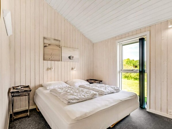 A bedroom with a bed, a nightstand, a window, and a wall-mounted shelf with decorative items.