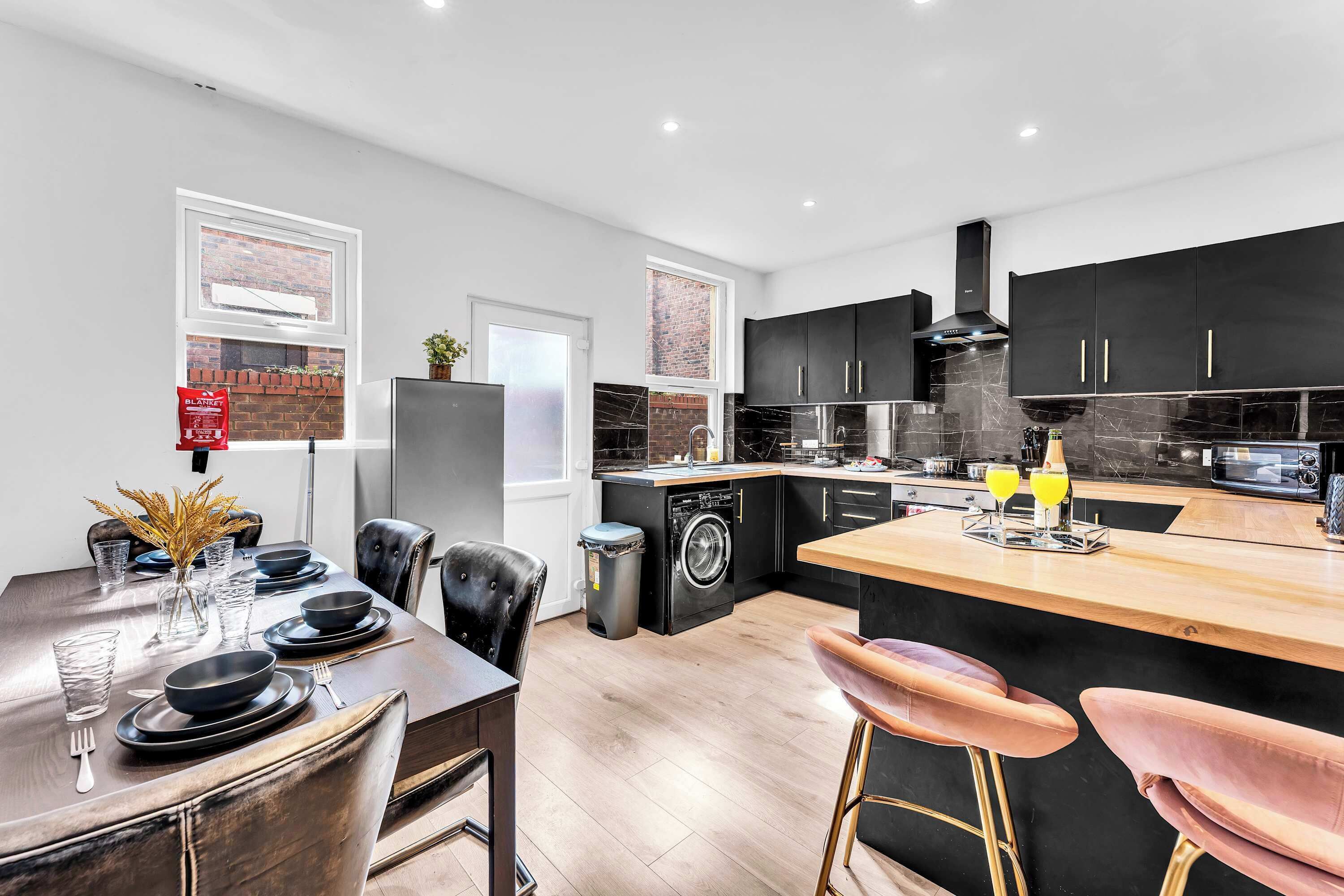 A modern kitchen with black cabinets, a wooden island, and a dining area with a table set for four.