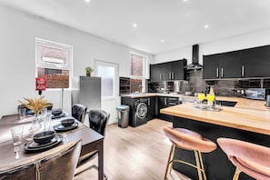Une cuisine moderne avec des meubles noirs, un îlot central en bois et un coin repas avec une table dressée pour quatre personnes.