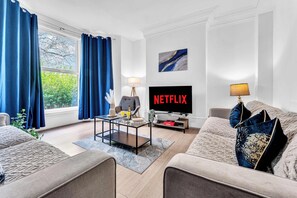 Un salon avec un canapé, une table basse, un téléviseur et des rideaux.